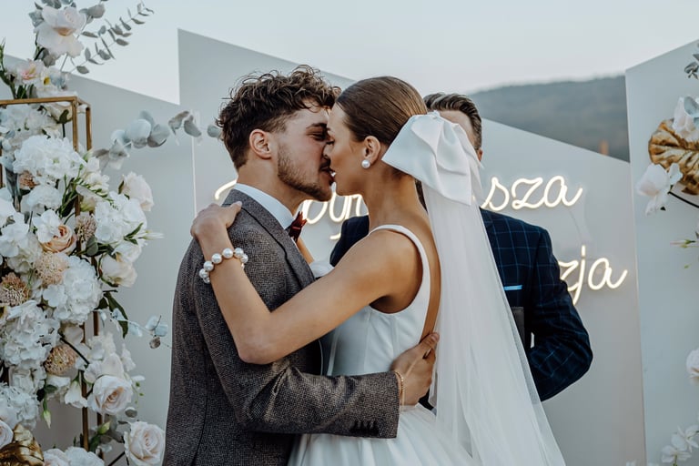 Bride and groom kissing at wedding ceremony with white floral backdrop and decorations
