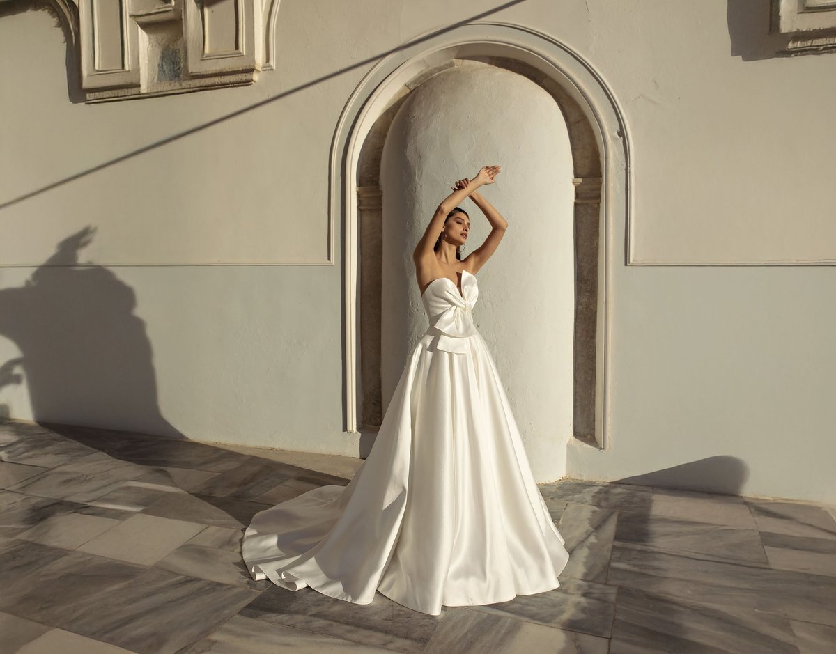 Woman in white flowing gown posing under arched doorway with hand raised to head