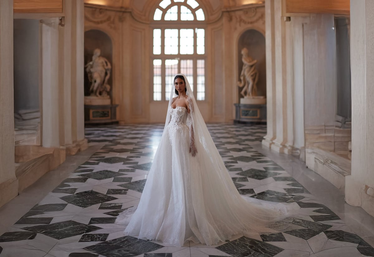 Bride in white wedding gown with long veil standing in ornate palace hallway with classical columns and geometric floor