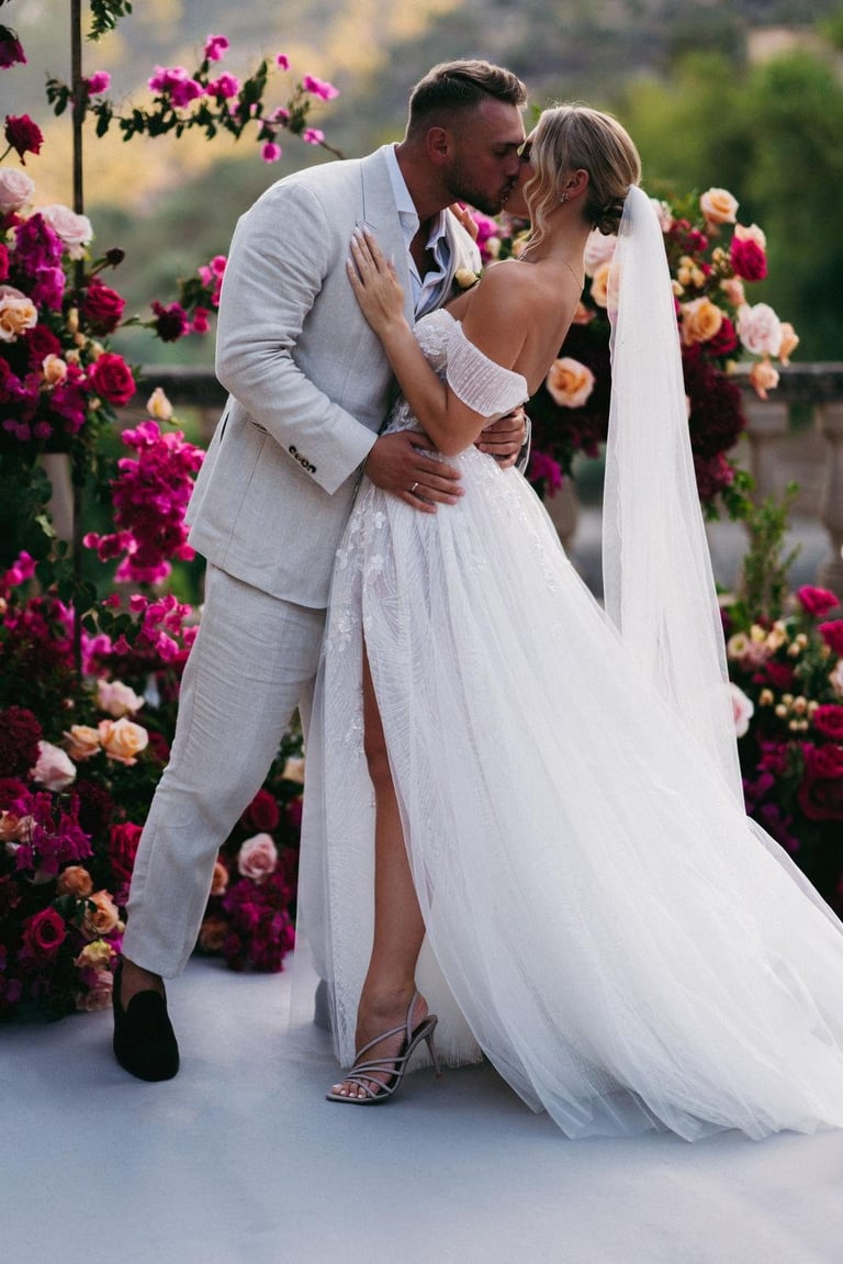 Bride and groom kissing at their wedding ceremony, surrounded by vibrant pink and peach flowers