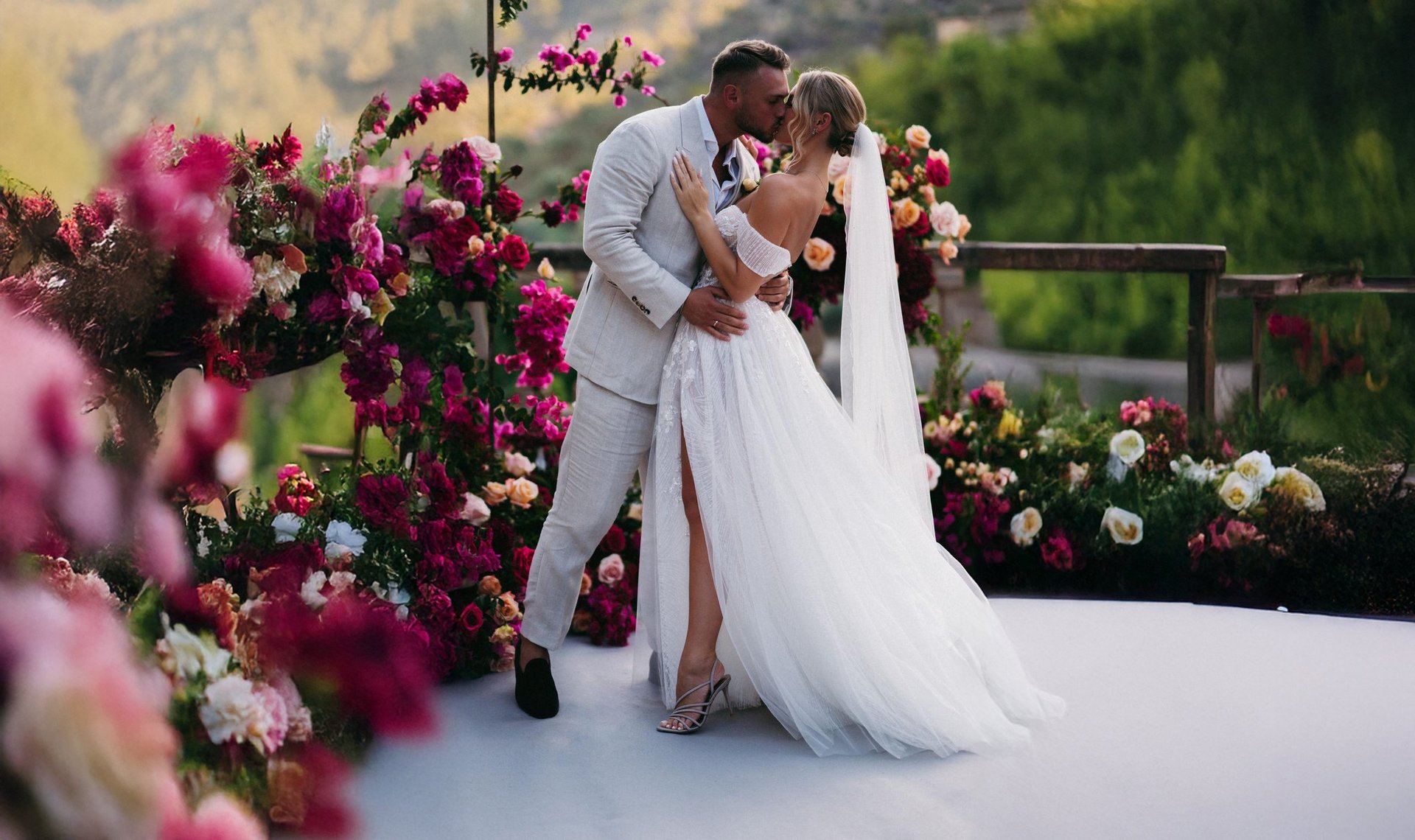 Bride and groom kissing on wedding day surrounded by pink and magenta floral arrangements