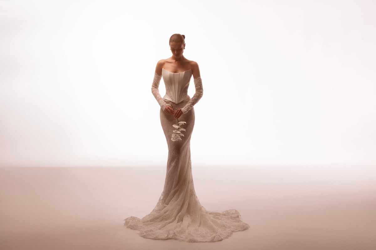 Woman wearing an elegant beige strapless gown with a long flowing train, standing against a neutral background.